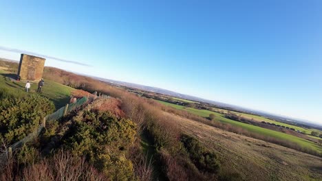 FPV-drone-flying-past-Billinge-hill-beacon-on-autumn-Lancashire-farmland-landscape