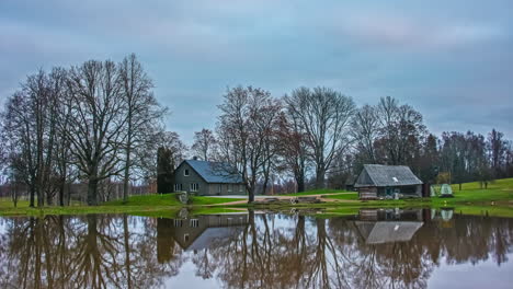 Timelapse-shot-of-wooden-cottages-beside-lake-throughout-the-cloudy-day-during-dry-autumn-day