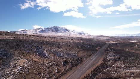 Luftaufnahme-Von-Epica-Road-Trip-In-Sierra-Nevada-Mit-Schneegipfelgebirgslandschaft-Und-Asphaltierter-Straße-Mit-Schnell-Fahrenden-Autos