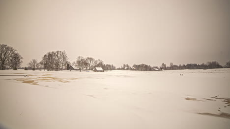 Timelapse-shot-of-snow-covering-ground-slowly-melting-along-rural-countryside-with-the-view-of-village-cottage-in-the-background