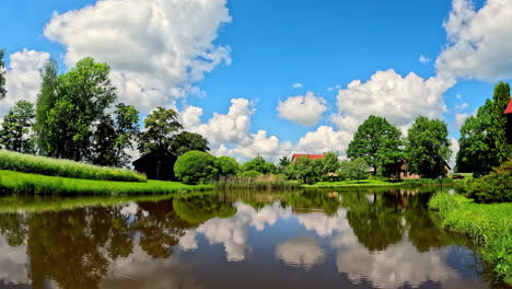 Large-fluffy-clouds-billowing-over-a-cabin-and-reflecting-off-the-surface-of-a-pond---time-lapse