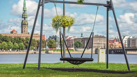 Timelapse-shot-of-an-empty-swing-beside-a-river-during-the-morning-time-with-the-view-old-buildings-in-the-background-on-a-cloudy-day