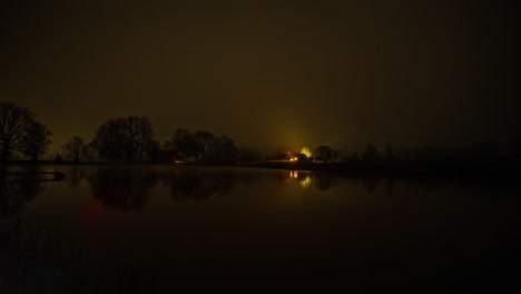 Timelapse-shot-from-night-to-morning-over-a-lake-in-the-foreground-with-a-small-wooden-cottage-in-the-background-along-rural-countryside