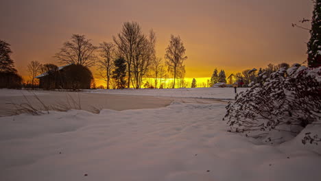 Orange-Sunset-behind-leafless-trees-during-snowy-and-icy-winter-day-in-nature---time-lapse-footage