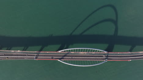 Aerial-top-down-shot-of-traffic-on-tied-arch-bridge-with-shadows-on-the-water-during-golden-hour