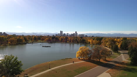 Aerial-shot-of-Denver,-Colorado-on-a-sunny-day-during-fall-with-colorfull-trees,-mountains,-skyscrapers-and-sunlight-reflecting-in-a-lake