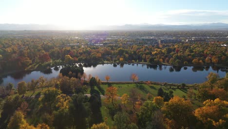 People-riding-and-walking-in-the-magnificent-autumn-landscape-of-Wash-Park-with-sunlight-shining-through-lake-water-and-mountain-range-in-the-background,-Denver,-Colorado