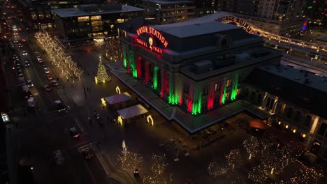 Denver-Union-Train-Station-Colorado-at-Evening-illuminated-During-Christmas,-Aerial-Backwards-View-of-Colorful-Lights-in-Downtown-District