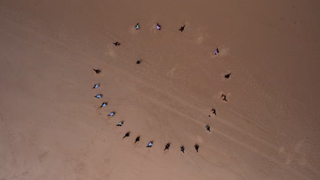 Topdown-ascending-shot-of-Surf-lesson,-People-in-a-circle-warm-up-on-Sand,-Orbiting-motion