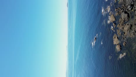 Vertical-video-of-rocky-coastline-in-Sanxenxo-flyover-calm-seascape-and-blue-sky,-Galiza
