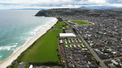 Dunedin-city-buildings-and-stadium-on-Pacific-ocean-coastline,-aerial-drone-view