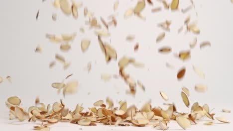 Sliced-raw-brown-almond-nut-pieces-falling-and-bouncing-into-pile-on-white-table-top-in-slow-motion