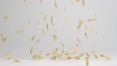 Slivered-raw-almond-nut-pieces-bouncing-into-pile-on-white-backdrop-in-slow-motion