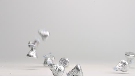 Silver-wrapped-chocolate-Hershey-candies-bouncing-into-pile-on-white-table-top-in-slow-motion