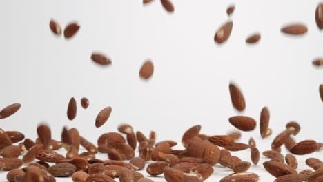 Whole-raw-almonds-bouncing-and-falling-into-pile-on-white-table-top-in-slow-motion
