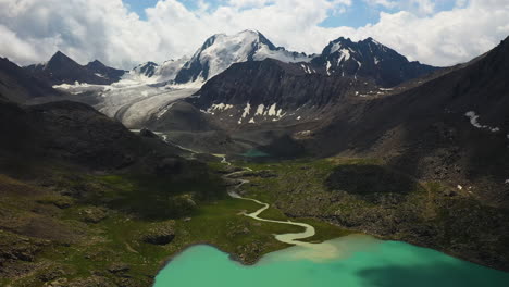 Toma-Aérea-De-Un-Río-Que-Atraviesa-Las-Montañas-Hasta-El-Lago-Ala-kol-En-Kirguistán