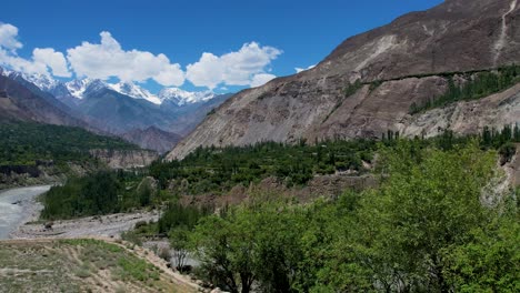 aerial-shot-of-the-Hunza-mountains-over-the-Indus-river,-the-green-town,-and-the-blue-sky-with-clouds