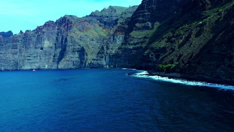 Blue-Sea-Water-With-Smooth-Waves-Under-High-Mountains-In-Tenerife-Island,-Spain