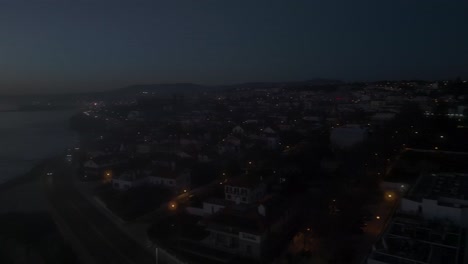 Aerial,-tracking,-drone-shot-of-marginal-at-the-coast-of-Estoril,-at-night-time-in-Lisbon,-Portugal