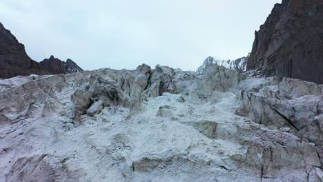 Aufschlussreiche-Drohnenaufnahme-Eines-Schneebedeckten-Felshangs,-Um-Den-Ak-Sai-Gletscher-In-Kirgisistan-Zu-Enthüllen