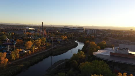 Aerial-drone-shot-revealing-Elitch-garden-theme-water-park-with-view-of-important-buildings-in-the-background-during-sunset,-Denver,-Colorado