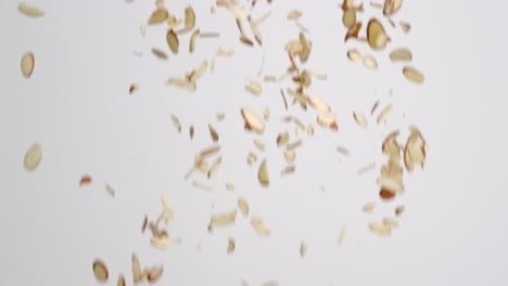 Sliced-almond-nut-pieces-raining-down-on-white-backdrop-in-slow-motion