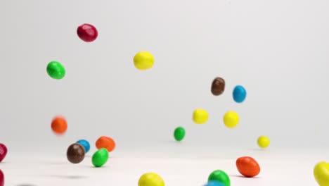 Bright-colored-chocolate-covered-peanut-m-and-m-candies-bouncing-around-on-white-table-top-in-slow-motion