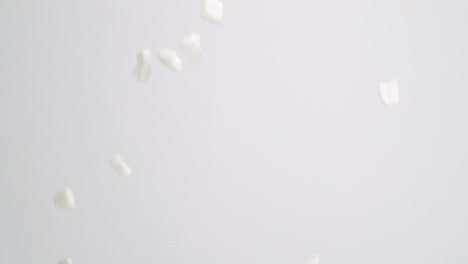 White-freeze-dried-coconut-chunks-raining-down-on-white-backdrop-in-slow-motion