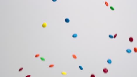 Bright-multi-colored-chocolate-covered-candies-falling-in-slow-motion-on-white-backdrop