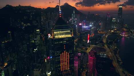 Aerial-drone-panning-pull-away-shot-of-Hong-Kong-skyline-with-Central-Plaza-building-in-foreground-and-Central-district-and-Mountain-range-in-backdrop-during-a-cinematic-and-colourful-sunset-afterglow