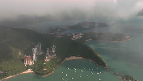 Aerial-drone-slow-pull-away-shot-of-South-Bay-Beach,-Hong-Kong-with-low-hanging-clouds-and-mooring-yachts