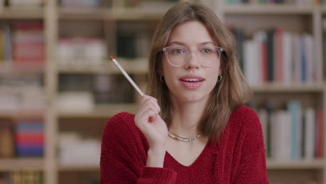 A-young-beautiful-female-student-holding-pencil-reacts-to-an-idea-in-the-library—medium-shot