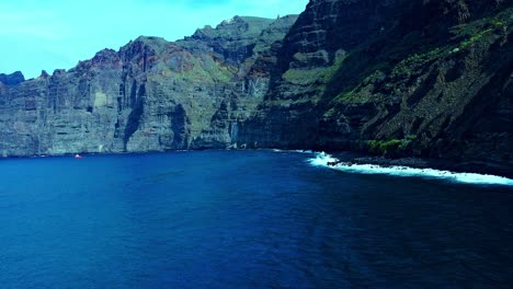 Blue-Sea-Water-With-Smooth-Waves-Under-High-Mountains-In-Tenerife-Island,-Spain