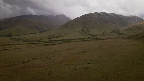 Wide-tussock-plains-at-the-foot-of-rugged-mountain-range-that-touches-heavy-storm-clouds-above