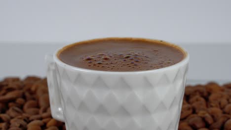 Türkischer-Kaffee-In-Einem-Weißen-Becher,-Umgeben-Von-Bohnen-Vor-Sauberem-Hintergrund