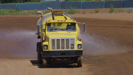 Yellow-water-truck-spraying-down-a-dirt-race-track-in-slow-motion