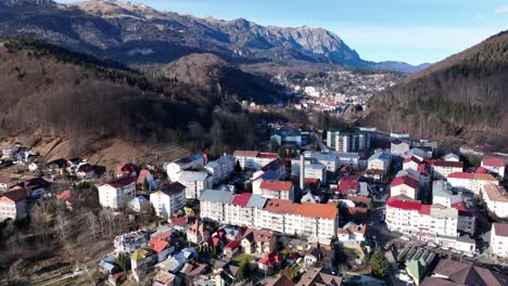Ascending-drone-shot-of-Sinaia-Village-in-Romania-during-sunlight-and-blue-sky-between-hills