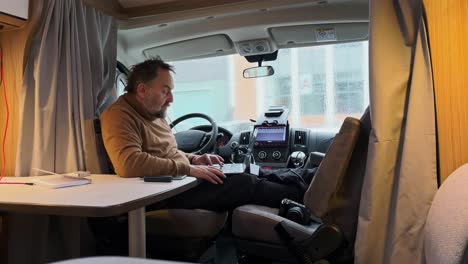 Senior-man-using-laptop-in-campervan,-digital-nomad-vanlife-concept