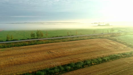Aerial-flyover-rural-fields-with-dew-and-clouds-at-road-with-cars-during-sunny-day-in-the-morning