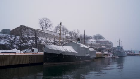 Covered-Boat-And-Navel-Vessel-Moored-At-Harbour-Beside-Akershus-Castle-During-Winter