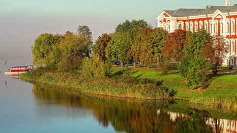 Beautiful-landscape-near-Jelgava-Castle-with-boats-anchored-near-a-pierce-along-the-river-bank,-and-a-piece-of-the-castle-seen-behind-the-trees