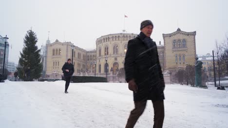Leute,-Die-über-Schnee-Mit-Dem-Norwegischen-Parlamentsgebäude-Im-Hintergrund-Gehen