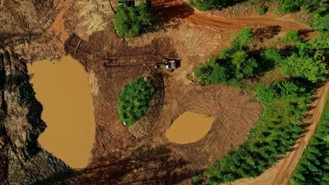 Aerial-drone-top-down-shot-over-yellow-excavator-truck-leveling-land-after-deforestation-during-daytime