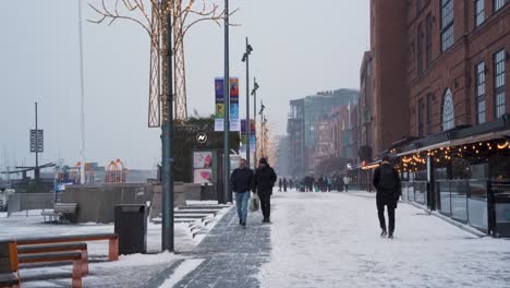 Gente-Caminando-Por-El-Paseo-Marítimo-De-Aker-Brygge-En-Oslo-Durante-El-Invierno-Y-La-Nieve-Cayendo