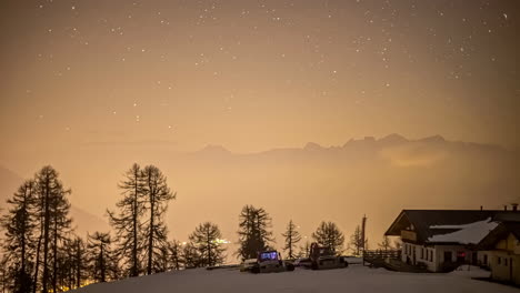 Time-lapse-shot-of-flying-stars-at-night-sky-with-yellow-atmosphere-on-snowy-mountaintop-with-ski-hut