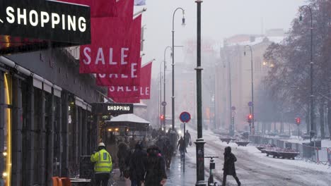 Shopping-Sale-Signs-Hanging-Above-Shops-Along-Karl-Johans-Gate-Road-During-Winter-Snow-Fall-And-People-Walking-Past