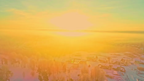 Aerial-flyover-snowy-winter-landscape-with-small-village-during-bright-golden-sunlight-sunset-at-horizon-illuminating-earth