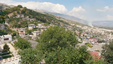 Scenic-pan-from-hilltop-to-picturesque-Gjirokaster,-Albania-village-on-sunny-day,-buildings-and-trees-in-view
