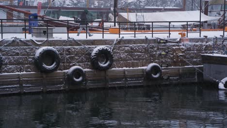 Schnee-Fällt-Auf-Gummireifen,-Die-An-Der-Wand-In-Aker-Brygge-Marina-Hängen,-Um-Boote-Zu-Schützen