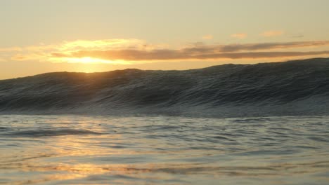 The-golden-glow-of-the-rising-sun-as-a-short,-heavy-wave-crashes